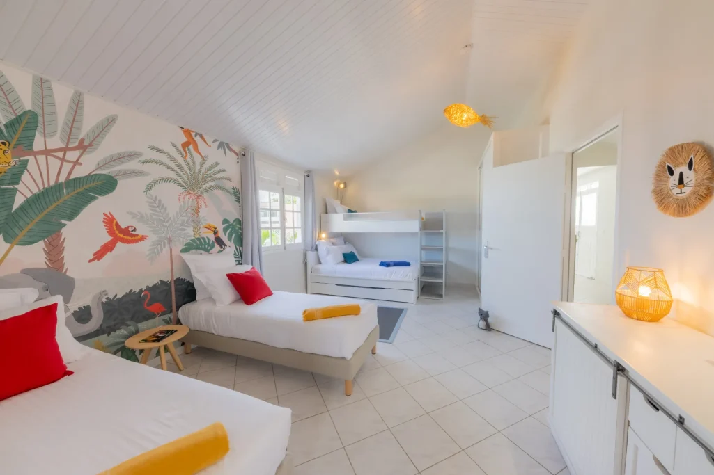 Chambre pour enfants composée de quatre lits, décor tropical et ambiance accueillante.