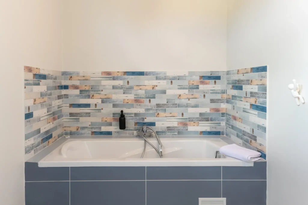 Baignoire moderne avec carrelage bleu et beige sur les murs. Serviette posée à côté.