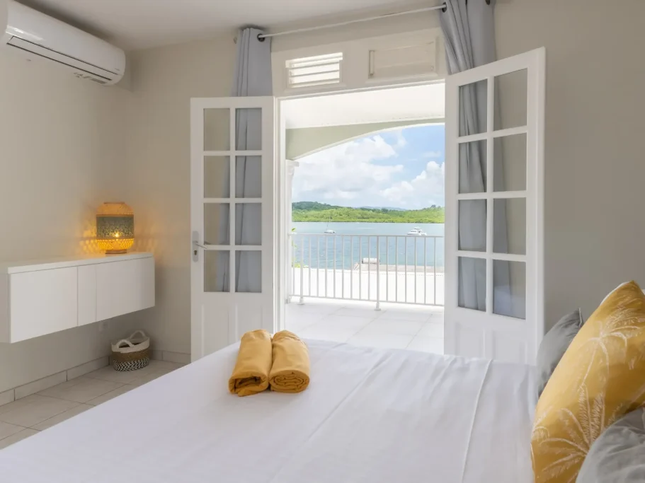 Chambre lumineuse avec fenêtres ouvertes donnant sur une vue de la mer.