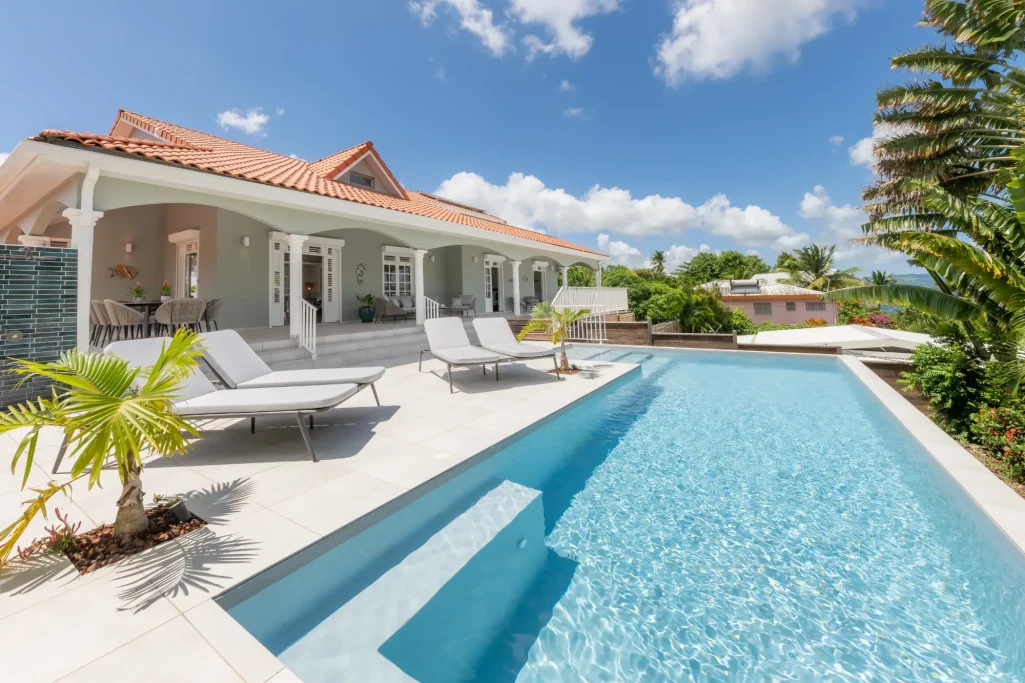 Villa moderne avec piscine, chaises longues et jardin tropical sous un ciel bleu.