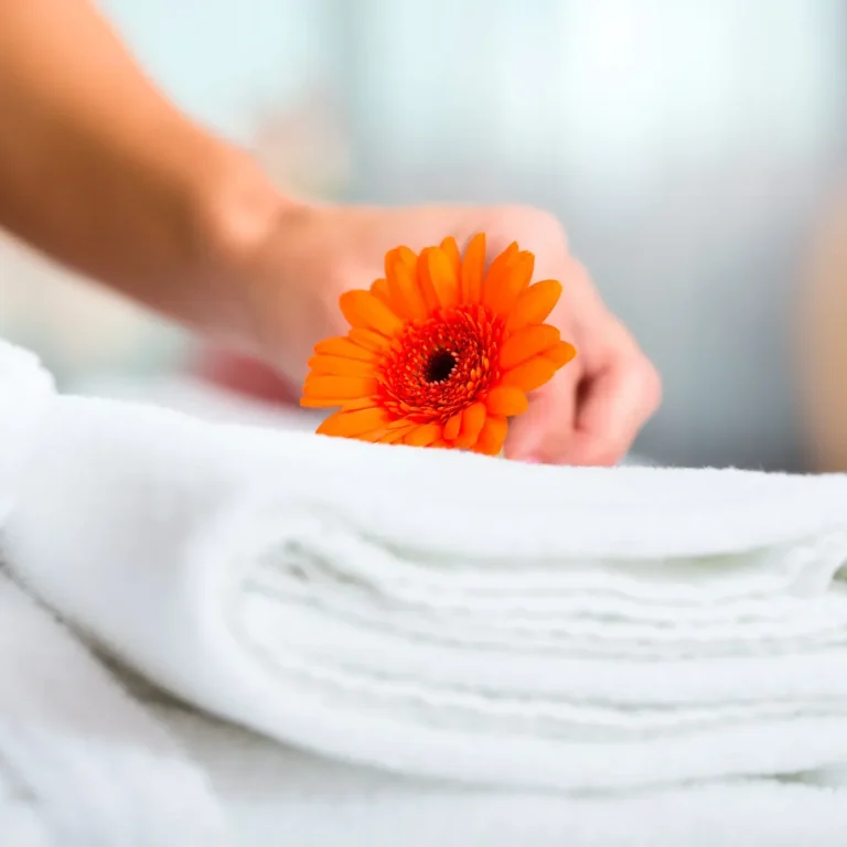 Main dans une serviette pliée, tenant une fleur orange.